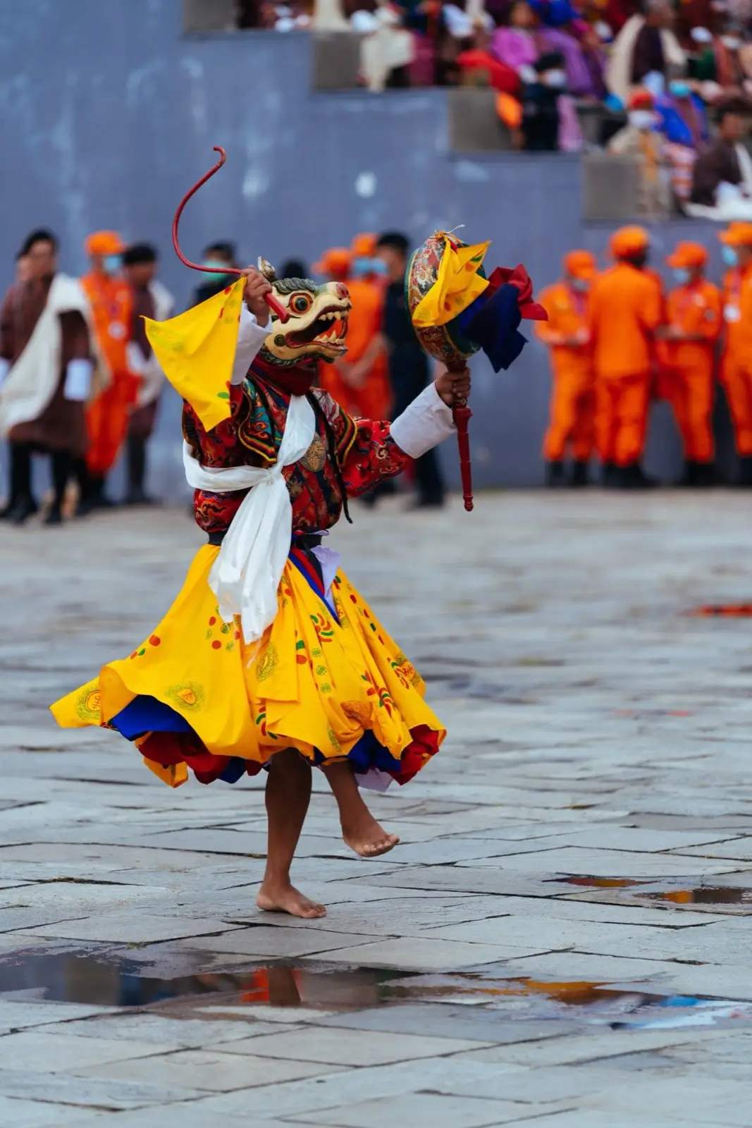Masked cham dancer in a swirling yellow costume at a tshechu festival